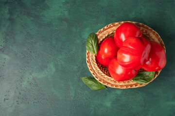 Wicker bowl with fresh ripe tomatoes and basil on green background