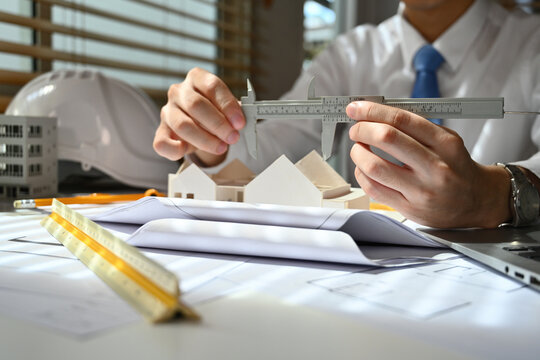 Close-up image of Engineer or architect man using vernier caliper to measure architectural model, check house model scale