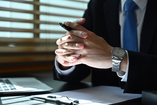 Close up image of Clasped hands of businessman in formal suit while sitting at office desk.