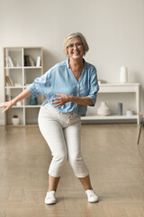 Cheerful carefree active retired woman dancing at home, enjoying motion, leisure, music,...