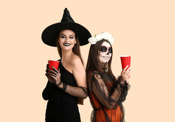 Female friends dressed for Halloween with drinks on beige background