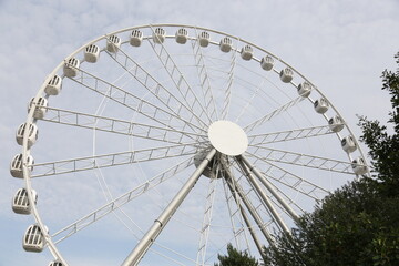 Fototapeta premium Modern white Ferris wheel in the central park against sky. Entertainment, attraction, amusement park. 