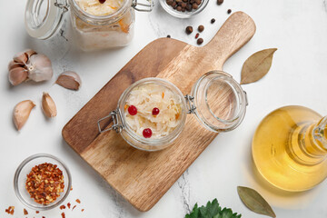 Wooden board with jar of delicious sauerkraut and different spices on white background