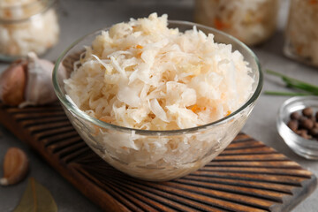 Wooden board with glass bowl of delicious sauerkraut on grey background