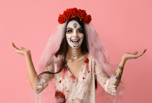 Beautiful young woman dressed as dead bride for Halloween party pointing at something on pink background