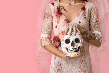 Young woman dressed as dead bride for Halloween party with painted human skull on pink background