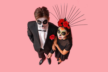 Young couple dressed for Mexico's Day of the Dead (El Dia de Muertos) on pink background - obrazy, fototapety, plakaty