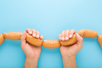 Young adult woman hands holding and showing string of raw fresh thick sausages for boiling. Light blue table background. Pastel color. Closeup. Point of view shot. Top down view. - Powered by Adobe