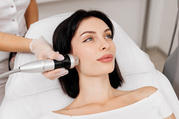 Young сaucasian woman undergoing a cosmetic procedure fractional RF lifting against a light...