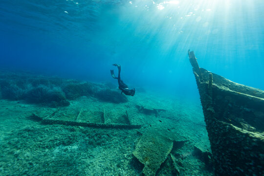Freediver diving towards a shipwreck at the bottom of the sea. Young man dIver eploring sea life.