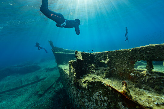Freediver diving towards a shipwreck at the bottom of the sea. Young man dIver eploring sea life.