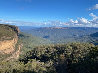 In the scene, a vast expanse of mountain ranges stretches to the horizon, with majestic peaks layered upon each other. Near the foreground, an individual stands atop a vantage point