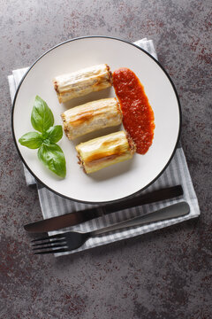 Baked leek stuffed with beef, rice, cheese and vegetables served with tomato sauce close-up in a plate on the table. Vertical top view from above