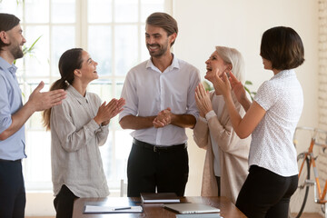 Five diverse businesspeople standing in boardroom clap hands congratulating team leader, best...