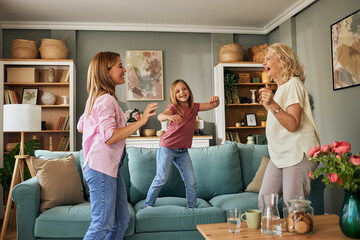 Overjoyed three generations of women dancing together in living room