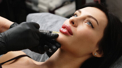 Close-up, woman's lips. A surgeon wearing medical gloves carefully and slowly injects hyaluronic...