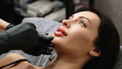 Close-up, woman's lips. A surgeon wearing medical gloves carefully and slowly injects hyaluronic...