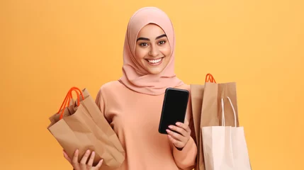 Schilderijen op glas Muslim Arab Woman wearing a hijab holding smartphone and bright paper shopping bags on a studio background Concept of Shopping, Black Friday sale and Cyber Monday online. © ND STOCK