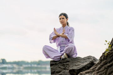 Kungfu master woman wearing kimono, practicing wushu sitting in lotus pose on stone