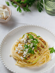Zucchini raw vegan pasta with avocado dip sauce, parsley leaves and feta cheese on white plate. On white background. Vegetarian healthy food. vertical