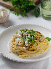 Zucchini raw vegan pasta with avocado dip sauce, parsley leaves and feta cheese on white plate. On white background. Vegetarian healthy food. vertical