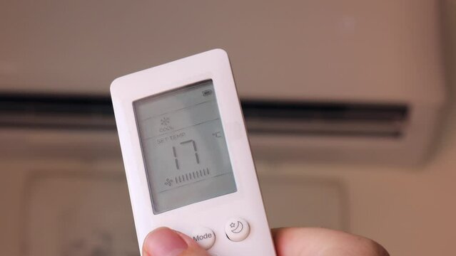 The girl holds a remote control to regulate the air conditioners temperature, ensuring a comfortable indoor environment during the hot summer.  backdrop of the air conditioner in the background