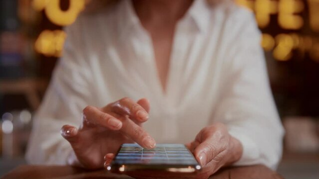 An old woman will scroll the photo on her smartphone with her hands. Senior female touches the phone screen with her fingers. Sitting in a cafe, using a mobile app. The concept of modern technologies