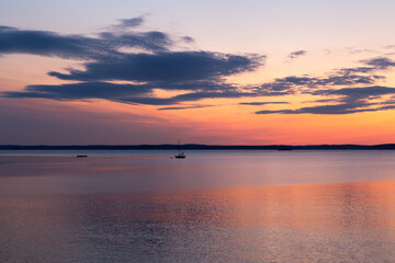 Tiny sailboat anchored in Frenchman Bay during a pink and orange sunrise, Bar Harbor, Maine, USA
