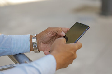 Detail of the hands of a Hispanic man with a mobile phone.