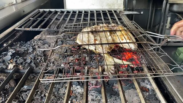 The pompano fish that has been cut in half is grilled over coals using charcoal at restaurant.