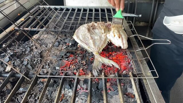 The pompano fish that has been cut in half is grilled over coals using charcoal at restaurant.