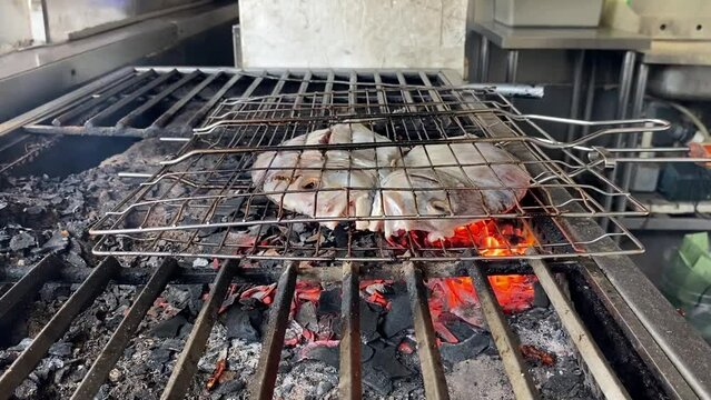 The pompano fish that has been cut in half is grilled over coals using charcoal at restaurant.