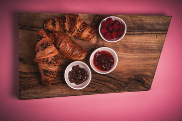 Croissants on the wooden board. Jam, chocolate, raspberries. Perfect French breakfast. Minimalistic photography. 