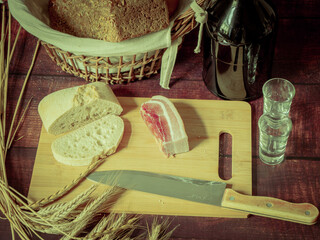 Rustic still life in antique style with bread, ears of wheat and ham and bacon. - 651622227