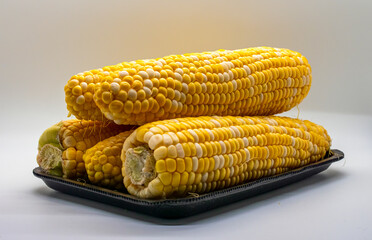 A Table Top View of Corn on the Cob, With a White Background, in a Black Tray