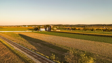 An Aerial View, in Late Afternoon, of Farmlands, Corn Fields, Silos, Barns and a single Rail Road...