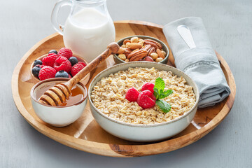Bowl of porridge or oatmeal with different ingredients on wooden tray. Breakfast serving.