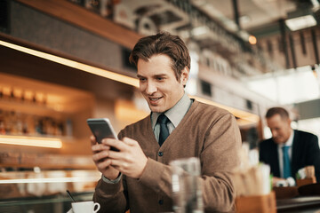 Young Caucasian business worker using his smartphone while having coffee in a caf? decorated for Christmas and the new year holidays