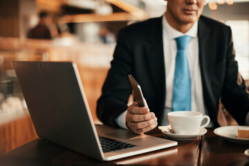 Middle aged businessman using a smartphone while having coffee in a cafe decorated for christmas and the new year holidays