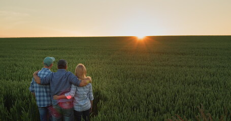 Happy family of farmers admiring the sunset over a field of wheat