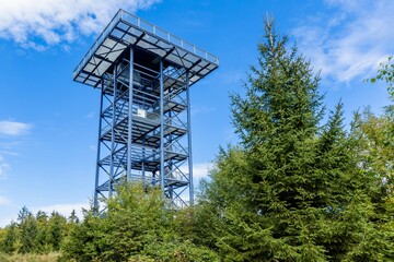 Lesna - Stara Knizeci Hut, Czech Republic - September 17 2023: View of the steel lookout tower named Havran standing in the forest surrounded with green trees. Sunny autumn day with blue sky.
