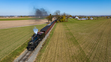 A Drone View From Above and In Front of a Steam Passenger Train Traveling Thru Farmlands and Blowing Smoke on a Sunny Fall Day