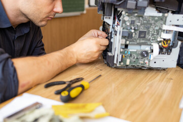 printer repair technician. A male handyman inspects a printer before starting repairs in a client's...