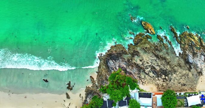 ..Aerial view scene of waves hitting the rocks at Patong beach Phuket..Waves lapping on the rocky beach in the bright green sea..The green sea lapping on the rocky beach in a white foam wave.