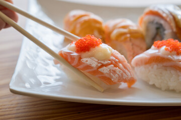 Chopsticks holding sushi. Salmon Roll. Hand holding sushi roll using chopsticks.