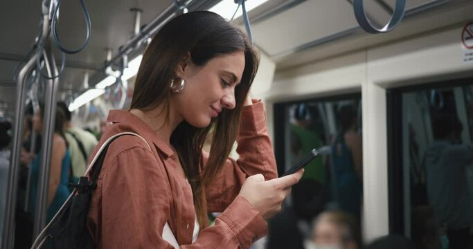 Mobile communication. Side view woman uses her smartphone typing message on phone for mobile communication with friends, family, colleagues through text messages apps, social media in subway train.