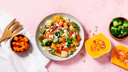 Autumn pasta salad with roasted pumpkin, broccoli, feta cheese on bright light gray background, vivid colors fall season salad, autumn food concept, top view