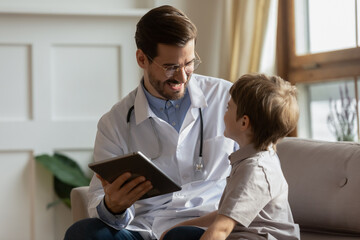 Smiling pediatrician using tablet at medical appointment with little boy, positive doctor wearing glasses filling patient card, anamnesis, showing good medical checkup results, children healthcare - obrazy, fototapety, plakaty