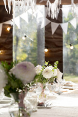 A long festive table decorated with white flowers and greenery; there are plates, glasses and candles on the table. The room is decorated with white garlands