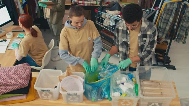 High angle view of one part of team sorting plastic bottles to containers while second part preparing clothes as humanitarian aid for poor people